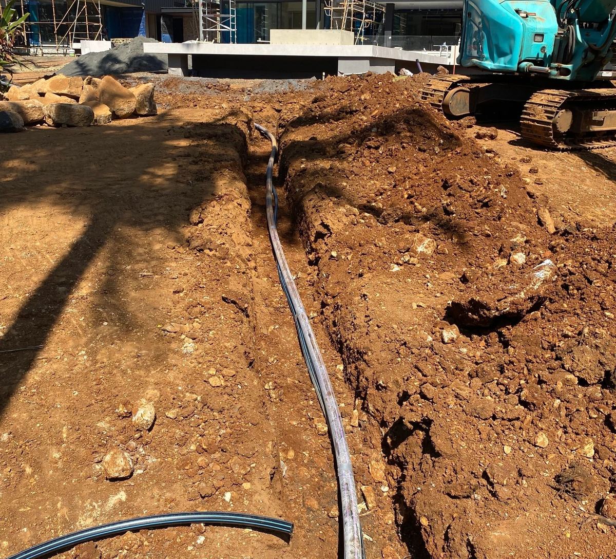 Irrigation main being laid in a trench on a job site, with an excavator working behind it.