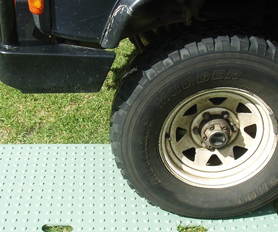 A four wheel drive wheel sitting on a green Polysource ground protection mat laid over grass.